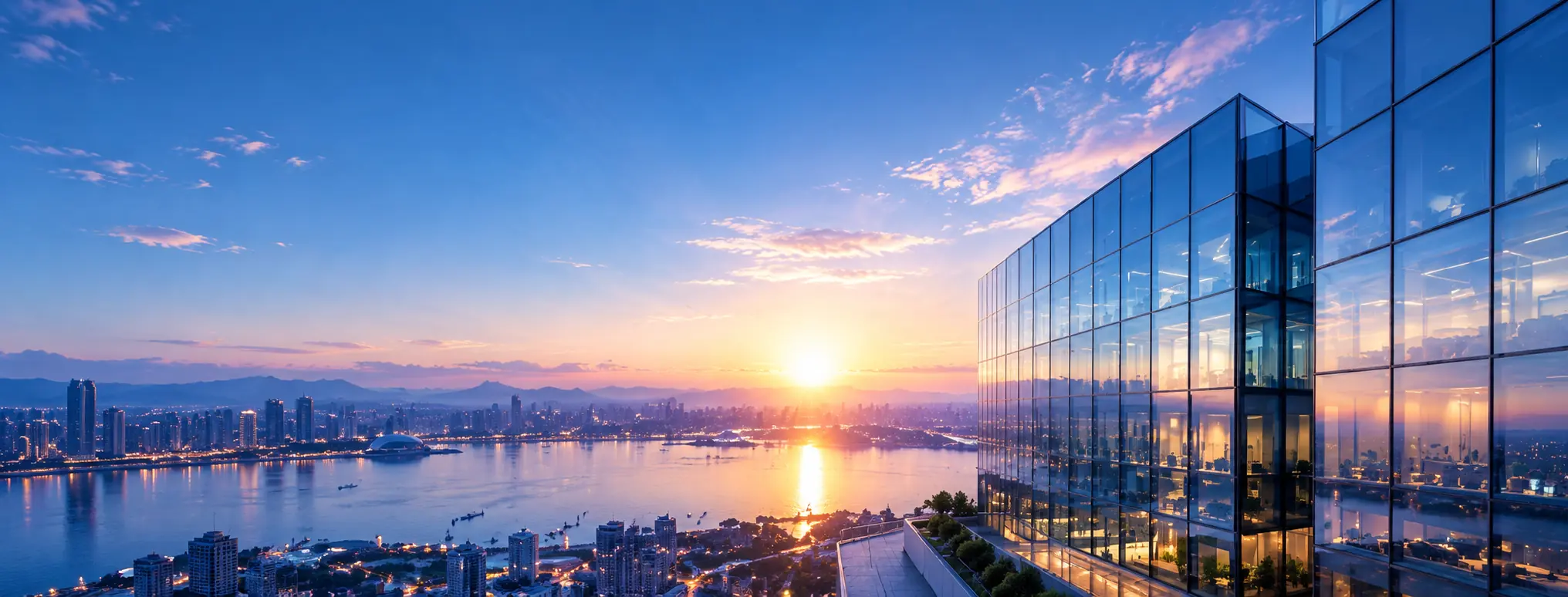 A modern glass office tower reflecting a sunset over the water